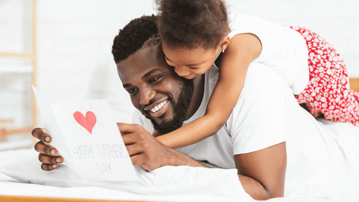 girl hugging dad while he holds a Happy Father's Day card