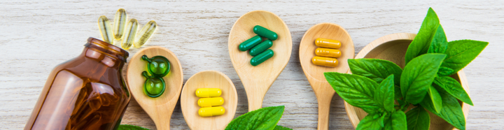 A few different colored supplements on wooden spoons and spilling out of a bottle